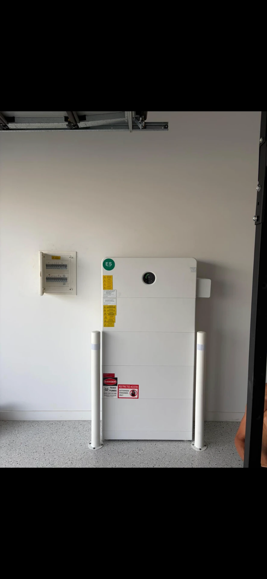 Stacked home battery unit beside a switchboard in a garage